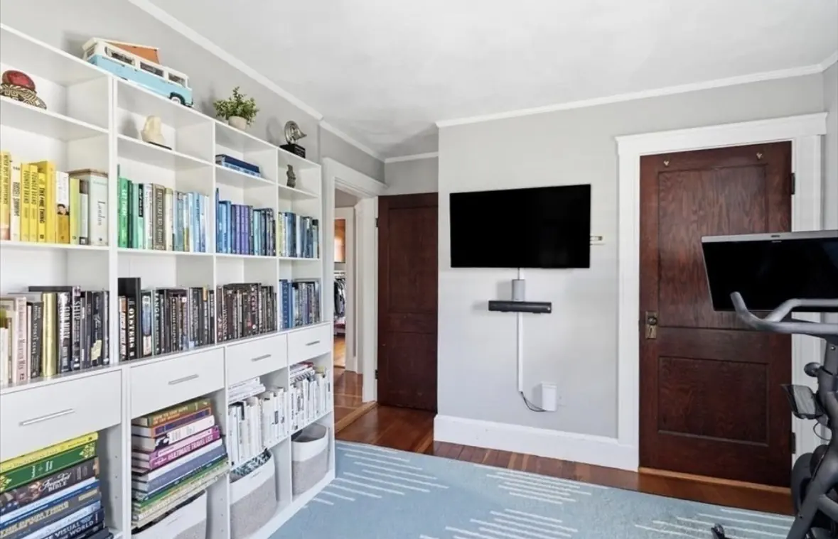 Den with built-in white bookshelves, wall mounted TV and hardwood floors
