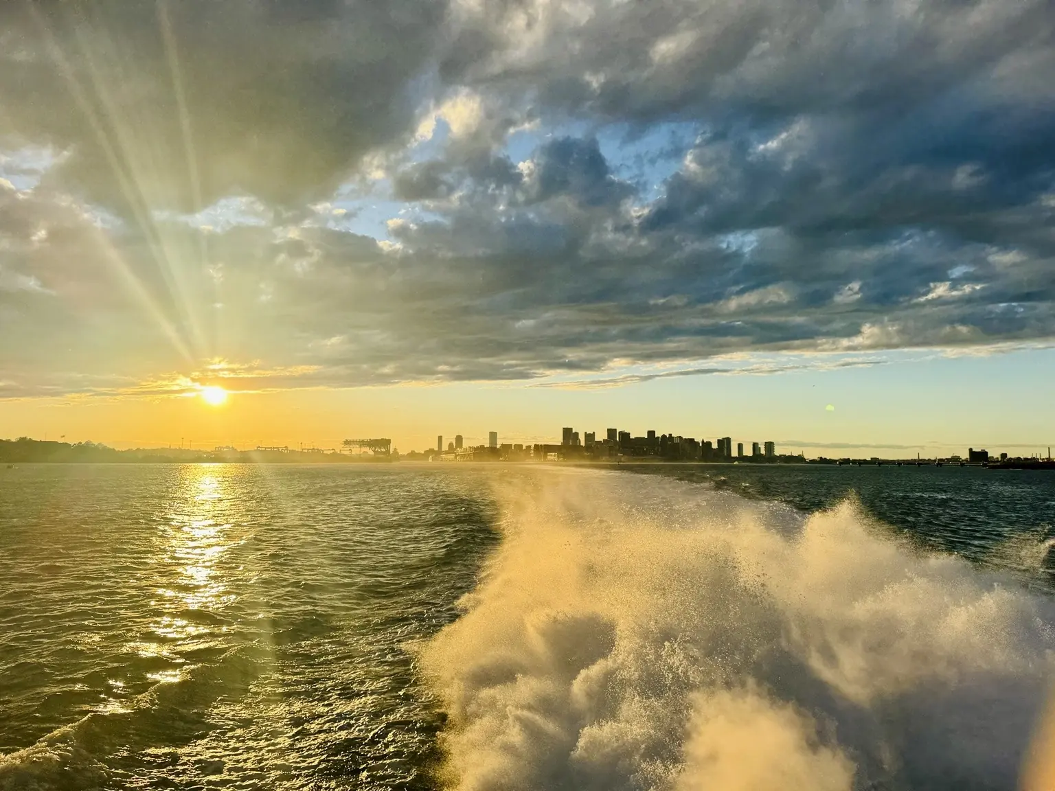 Ferry wake across Boston Harbor at sunset with the city skyline ahead