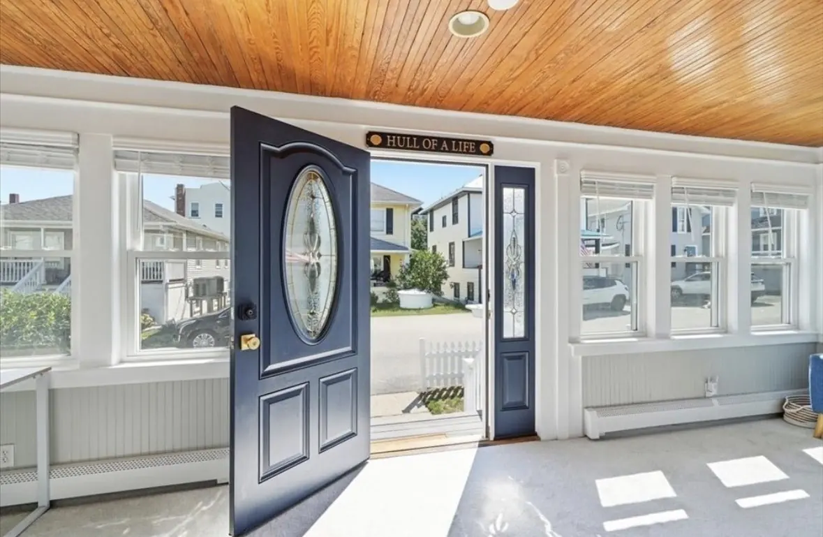 Enclosed sunroom entry with wood-paneled ceiling and open front door